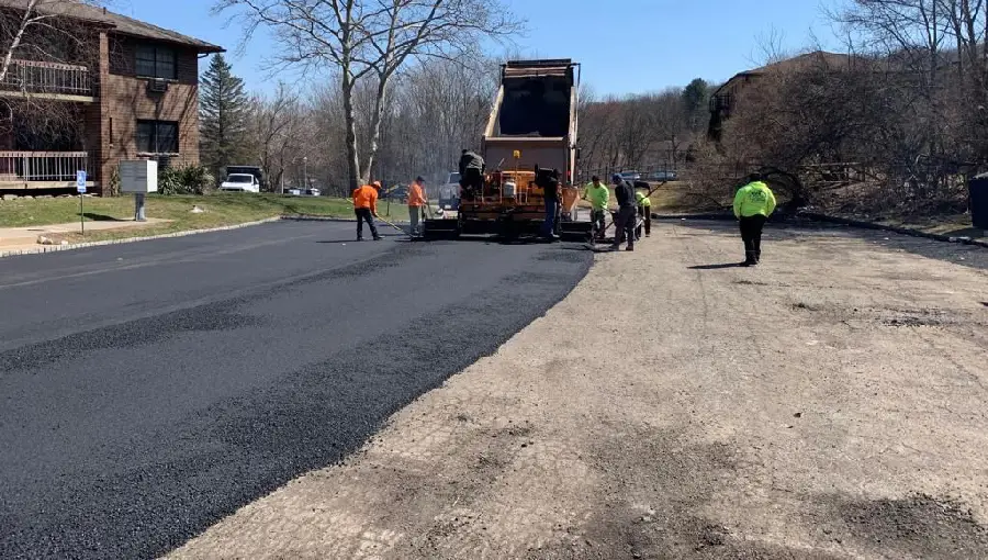 Commercial asphalt paving in progress in New Jersey, showing a large parking lot installation with heavy equipment and paving crew.
