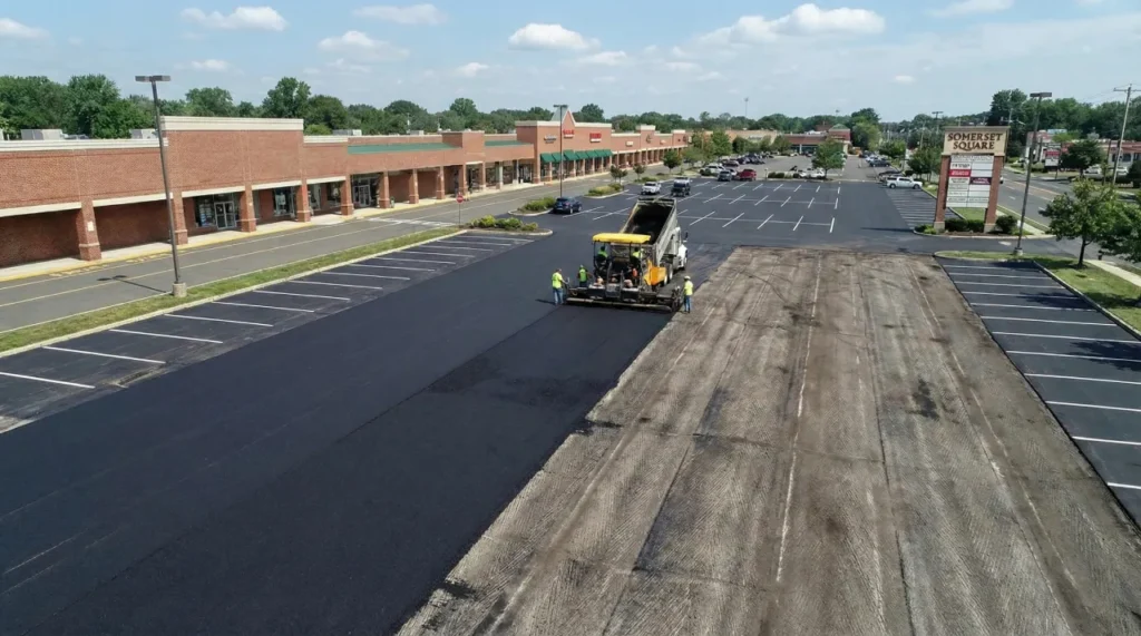 Aerial view of a commercial paving crew and heavy machinery laying new asphalt on a large parking lot at Somerset Square, illustrating the scope of a project like paving a 2-acre parking lot in Somerset County, NJ.