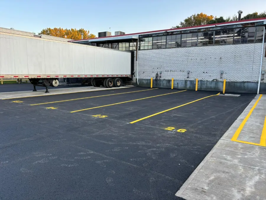 A professionally paved commercial loading dock with fresh black asphalt and clearly marked yellow spaces, demonstrating the curb appeal and durability needed for a large-scale investment subject to heavy truck traffic.