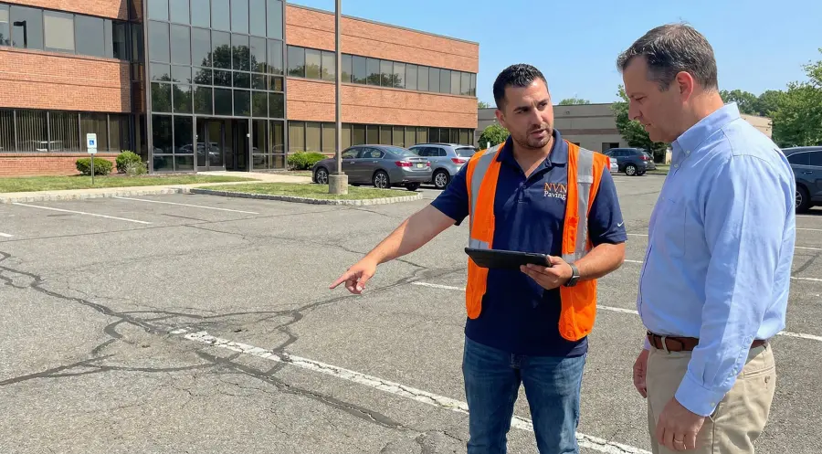 An NVN Paving representative conducts a professional site evaluation, pointing out asphalt cracks to a commercial client in a New Jersey office parking lot.